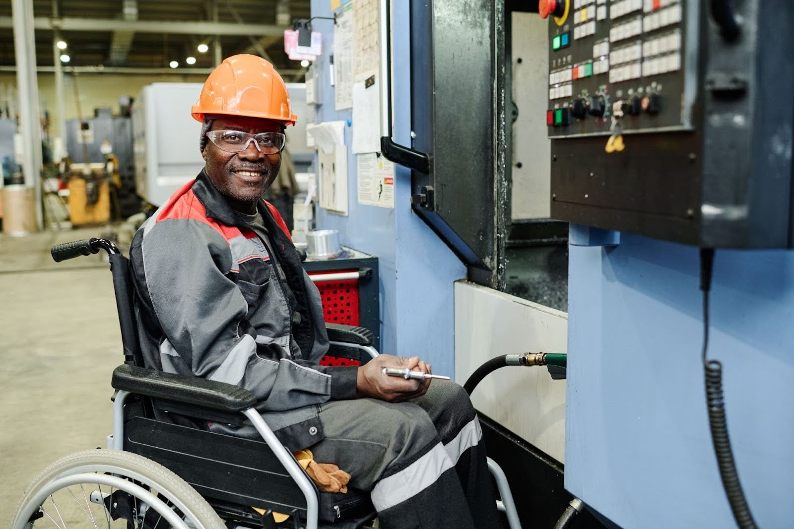 An employee in a hardhat, protective eyewear, and wheelchair who is smiling while on the clock because his employer is making him feel empowered this National Disability Employment Awareness Month.