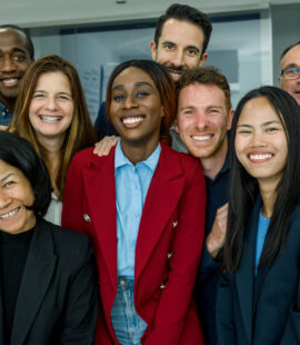 A diverse group of employees smiling in an office at a company they love working at because their employer learned how to retain talent in the workplace.